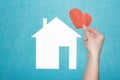 Concept of love in family and at home. hand holds red heart over white paper house on blue background. Insurance of real estate