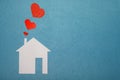 Concept of love in house. White paper house on blue textured background with red hearts from pipe. Royalty Free Stock Photo