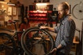 Concept of maintenance of bike. Concentrated cycling mechanic male repairing bicycle wheel working in garage with dark Royalty Free Stock Photo