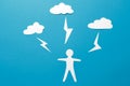 The concept of man is under threat. A paper man origami stands under lightning from the clouds on a blue background Royalty Free Stock Photo