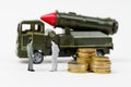 On a white surface are figurines of people, coins and a toy military vehicle. Royalty Free Stock Photo