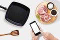 Concept of mockup using smartphone and raw pork chop steak, grill pan and spatula set isolated on white background. Clipping Path Royalty Free Stock Photo