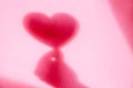 Concept modern abstract background of shadow heart in hand on a pink wall