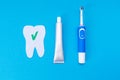 The concept of modern dental care products. Electric toothbrush, toothpaste, a tooth cut out of felt with a green ok icon. Blue