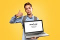 Concept of modern technologies and education. Caucasian teen boy holding open laptop and showing thumbs up. Yellow background. Royalty Free Stock Photo