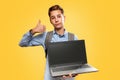 Concept of modern technologies and education. Caucasian teen boy holding open laptop and showing thumbs up. Yellow background. Royalty Free Stock Photo