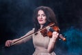 Beautiful brunette girl in a light beige dress playing the violin. Concept for music news. Smoky background. Royalty Free Stock Photo