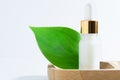 Natural cosmetics: serum with dropper and green leaves on white background