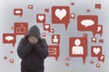 A concept of the negative effects of social media. A hooded man holding his head in his hands. With social media icons surrounding