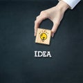 Concept of new ideas. Female hand holds a wooden block with a glowing light bulb. Dark background Royalty Free Stock Photo