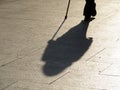 Person walking with a cane, black silhouette and long shadow on pavement