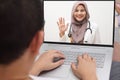 Concept of online medical healthcare, shows laptop display with Asian muslim female doctor smiling, telehealth, telemedicine video
