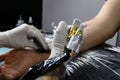 A tattoo artist fills a drawing on a man`s hand with a typewriter. The concept of overcoming pain, courage, creativity and