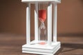 The concept of passing time. White hourglass with red sand inside on a wooden textural background. Royalty Free Stock Photo