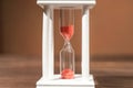 The concept of passing time. White hourglass with red sand inside on a wooden textural background. Royalty Free Stock Photo