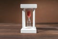 The concept of passing time. White hourglass with red sand inside on a wooden textural background. Royalty Free Stock Photo