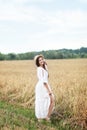 The concept of peace of mind. An attractive young woman stands in a golden wheat field holding a hat. The girl looks with a slight Royalty Free Stock Photo