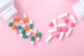 Different colorful drugs falling from two white  bottles on pink paper background. . Flat lay Royalty Free Stock Photo