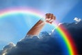 Divine hand god holding rainbow in fist out of clouds