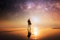 A concept picture of man holding a surfboard, silhouetted against the setting sun with stars and the universe overhead at night