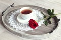 The concept of pleasant congratulations on solemn events. A red rose lies near a cup of tea on a white napkin, side view, gray Royalty Free Stock Photo