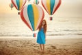 Concept portrait of little child girl with red hair and freckles standing on a beach with colourful hot air balloon Royalty Free Stock Photo