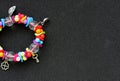 Concept For Postcard Or Invitation. Bracelet With Colorful Beads And Silver Charms In A Side Of Image On Black Background