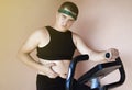 Cheerful fat man in a funny tracksuit is engaged in a stationary bike. The concept of problems with weight, losing weight, playing Royalty Free Stock Photo