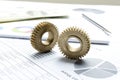 Closeup of two golden gears on the business documents, stack of money and pen