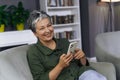 Concept reflects modern technology, communication, and happiness. Cheerful mature woman is sitting comfortably on a sofa Royalty Free Stock Photo