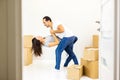 Picture of a cheerful couple dancing after moving into their new apartment with piles of cardboard boxes. Door blurred