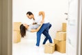 Picture of a cheerful couple dancing after moving into their new apartment with piles of cardboard boxes. Door blurred