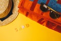 Concept of relaxing on the beach. inscription sand on a yellow background with sunglasses, a towel and a straw hat. top view