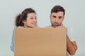 Funny wife and husband hiding behind the big carton box, together, looking foolishly. Man is bored.