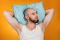 The concept of rest. Man, folding his hands under his pillow, sleeps overuses to the side. Orange background