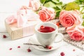 The concept of romantic tea. Wrapped gift, hibiscus tea, a bouquet of delicate roses, sweets Royalty Free Stock Photo