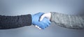 The concept of a safe handshake. Shaking hands in medical gloves on gray background.