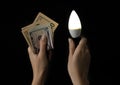 The concept of saving electricity. economical light bulb and money in the hands on a black background