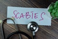 Concept of Scabies write on sticky notes with stethoscope isolated on Wooden Table