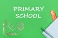 Text primary school, school supplies wooden miniatures, notebook on green background