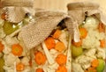 Concept of seasonal pickles jar with colored green raw tomatoes, orange carrot and white cauliflower on natural wooden background.