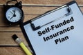 Concept of self-funded insurance plan write on clipboard isolated on Wooden Table Royalty Free Stock Photo