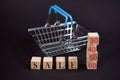 The concept of shopping. Wooden cubes with the word Sale and discount percentages on a dark background with a shopping cart