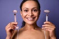 Middle aged pretty woman smiles toothy smile showing her face posing with jade stone roller massage on violet background with copy