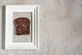 Concept. Slice of brown bread in a white photo frame on a concrete gray wall. Creative food poster