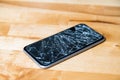 Concept of smart phone with broken screen. Top view on wooden desk background. Cracked, shattered lcd touch screen on modern Royalty Free Stock Photo