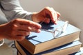 The concept of spending time reading books by elderly people. Reading glasses in hands on a stack of books, gray background, space