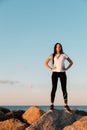 The concept of sport and a healthy lifestyle. A young woman in sportswear , standing on the coastal rocks, hands on hips. Copy Royalty Free Stock Photo