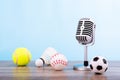 Concept sports commentator : The retro microphone put on the wooden table with football or soccer , tennis ball , baseball and