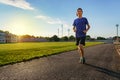 Concept of sports and health - teen boy runs along the stadium track, a soccer field with green grass Royalty Free Stock Photo